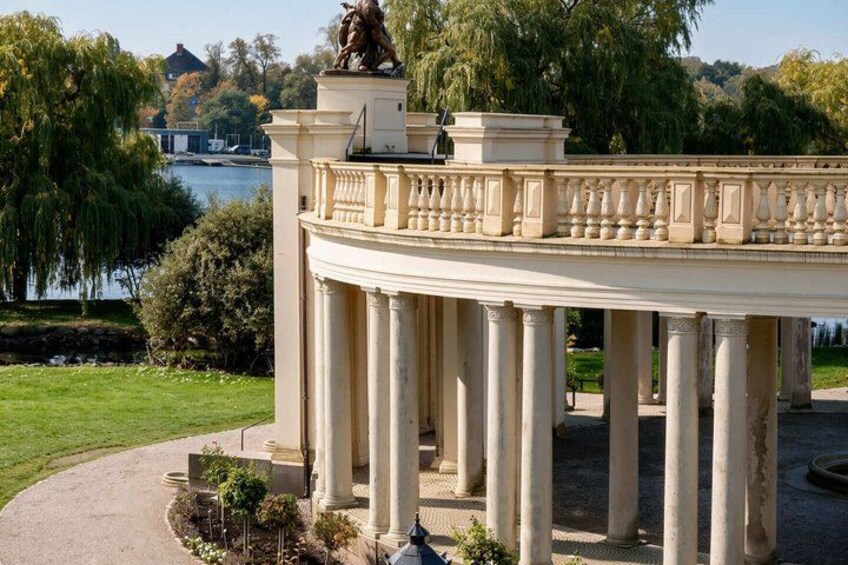 A classical pavilion with columns, a statue, and a lake in the background. 5