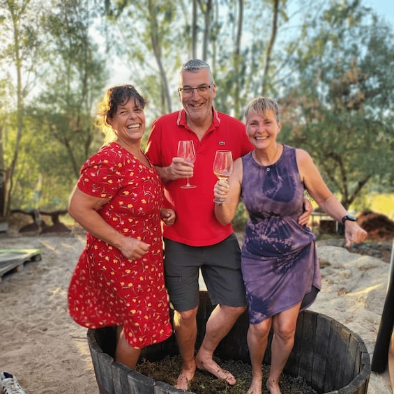 Three people standing in a wooden tub outdoors with trees in the background. 4