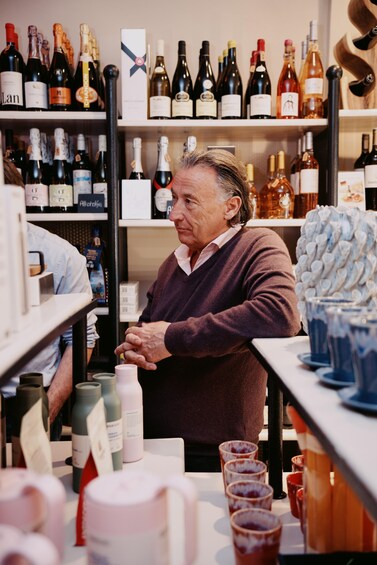 A person in a sweater standing in a store with shelves of wine bottles. 3