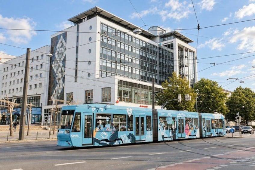 A tram with advertisements, a modern building, and a clear sky. 3