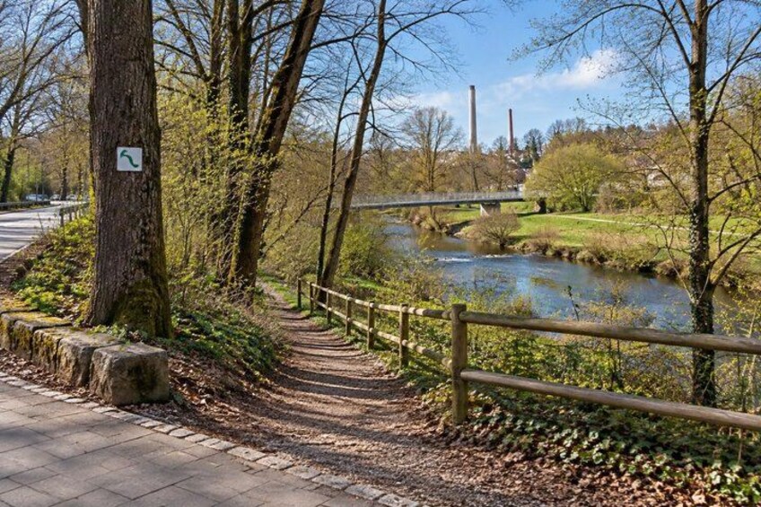 A paved path alongside a river, a wooden fence, and a bridge in the background. 3