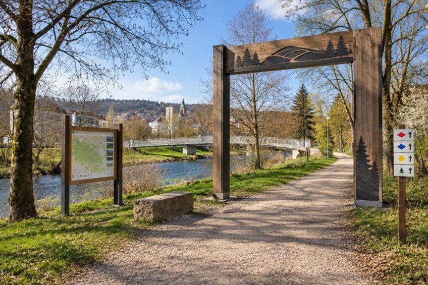 A gravel path leading through a park with a wooden archway, a river, and a bridge in the background. 4