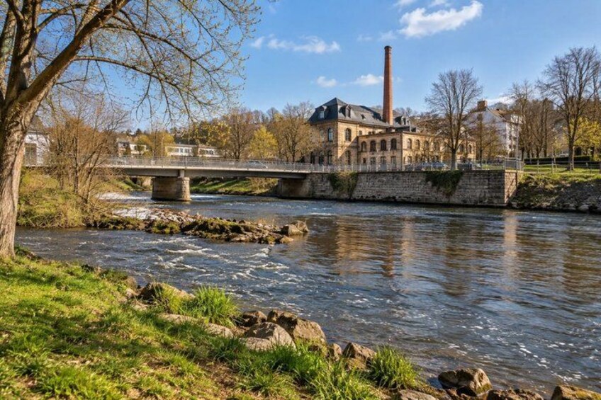 A river with a bridge, a building with a chimney, and a tree. 5