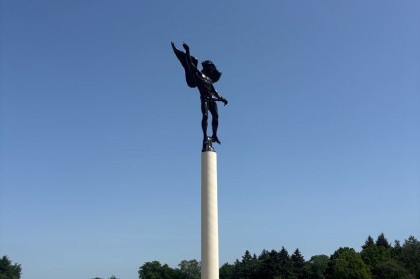 A statue of a person with raised arms on a tall white column, surrounded by trees. 4