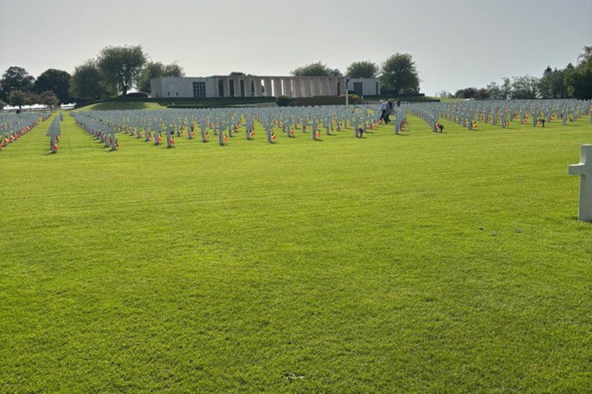A cemetery with rows of white crosses and a building in the background. 5