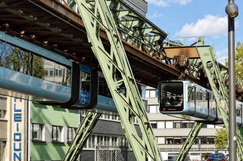 A train on an elevated track, a green metal structure, and a building with 'LE LION' signage. 3