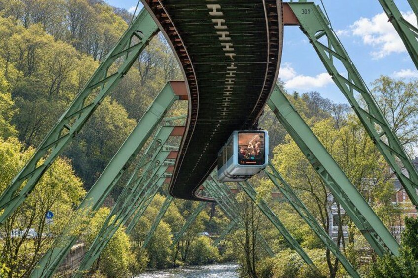 A green metal bridge with a pedestrian walkway, surrounded by trees and a river. 5