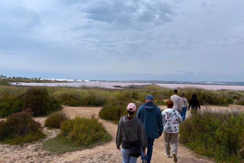 A group of people walking on a sandy path through a coastal landscape with dunes and a beach in the background. 2
