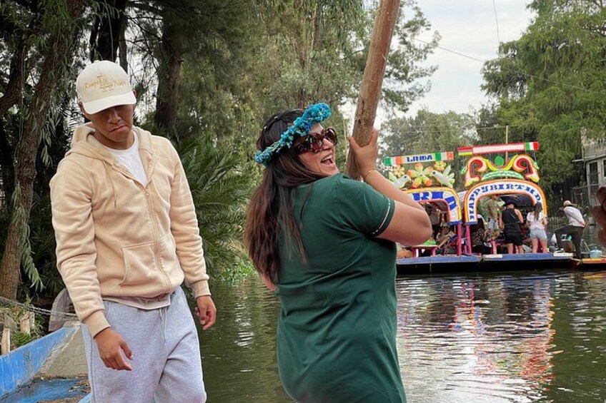 A person in a green shirt and blue headband standing on a boat, with another person in a beige jacket and white cap on a dock. 1