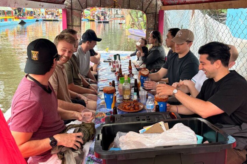 A group of people sitting at a table on a boat, enjoying drinks and food. 5