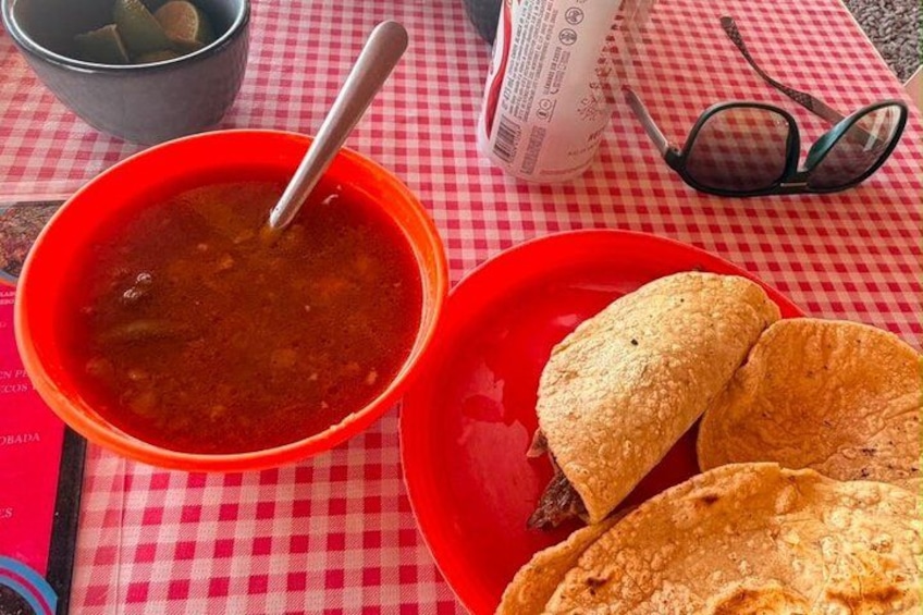 A red bowl of soup, a red plate with two tortillas, a pair of glasses, and a menu on a checkered tablecloth. 3