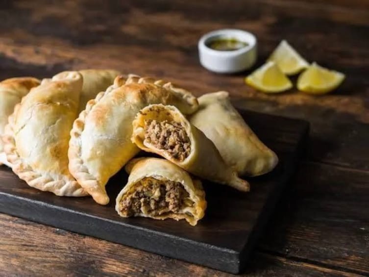 A plate of empanadas with a dipping sauce and lemon wedges. 2