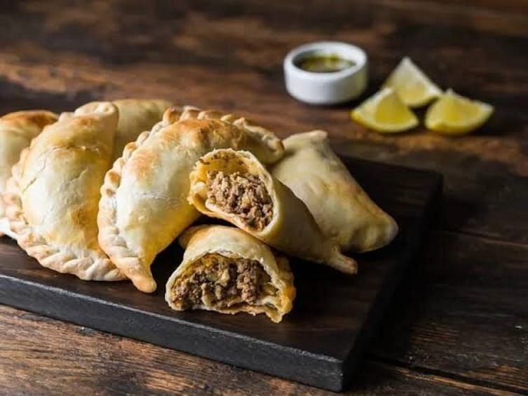 A plate of empanadas with a dipping sauce and lemon wedges. 2