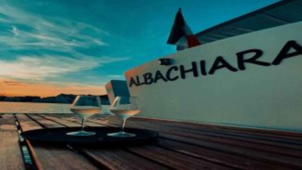 A boat with the name 'ALBACHIARA' on its side, a wooden deck, and two glasses of wine. 3