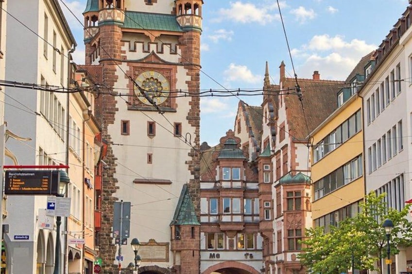 A historic building with a clock tower, surrounded by modern buildings and a clear sky. 2
