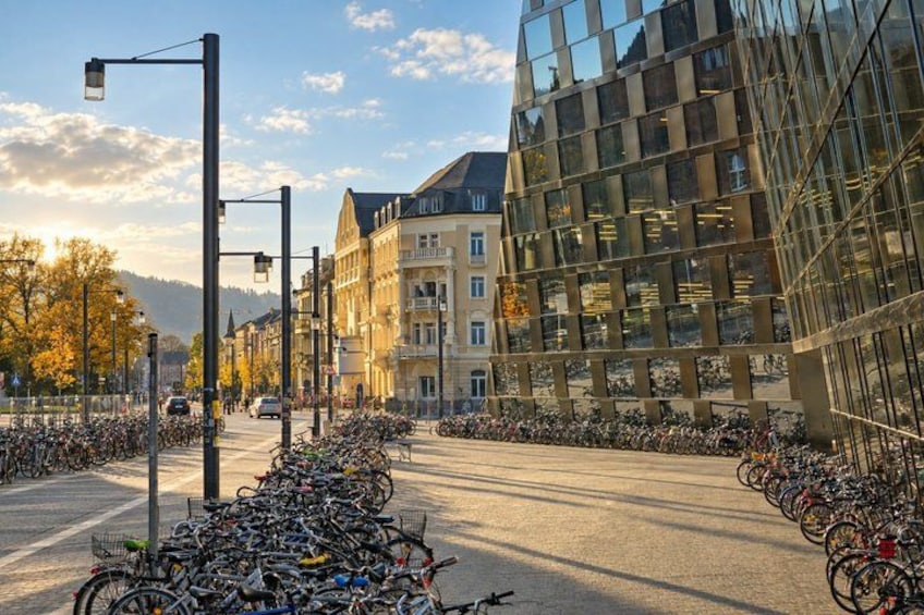 A street lined with parked bicycles, a modern glass building, and traditional architecture. 4