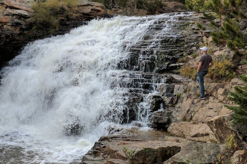 A waterfall cascading over rocks, a person standing on a ledge, and surrounding vegetation. 4