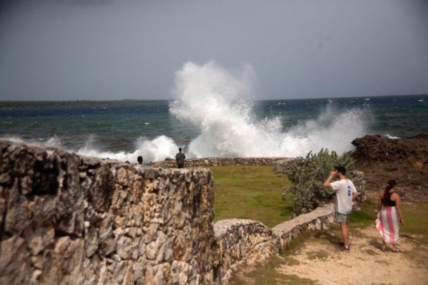 A rocky coastline with waves crashing against the shore, a person taking a photo, and another person standing nearby. 2