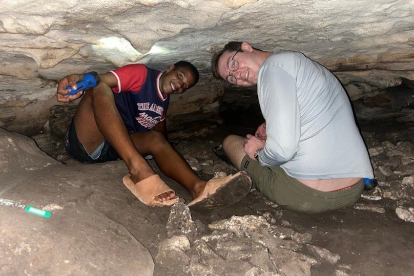 Two people sitting on the ground in a cave with rocky walls. 5