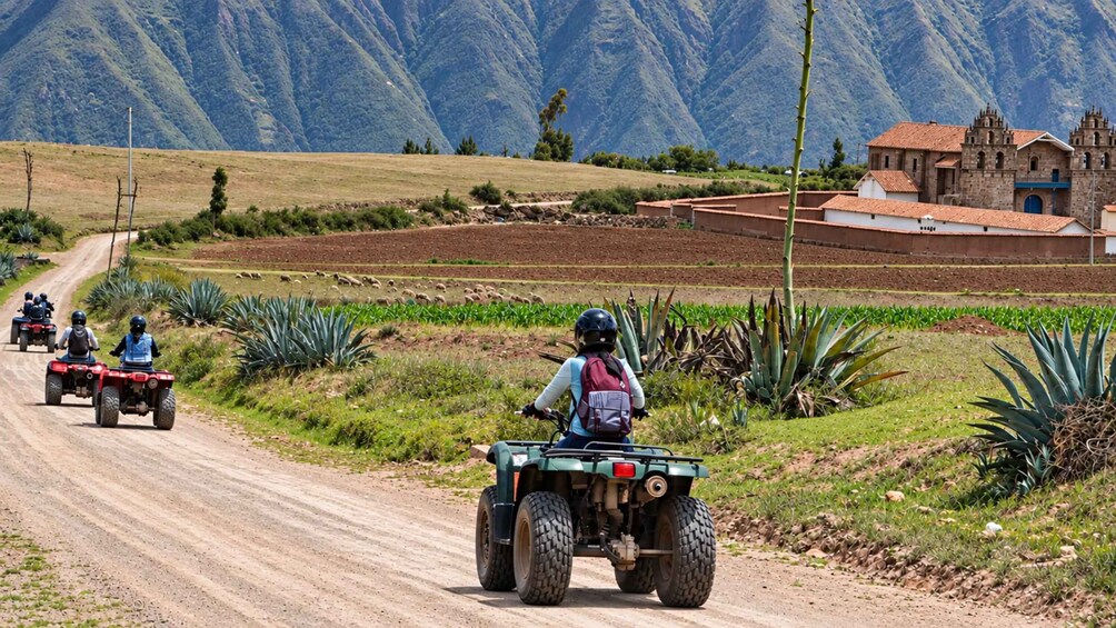 A dirt road with off-road vehicles, agricultural fields, and a mountainous landscape. 5