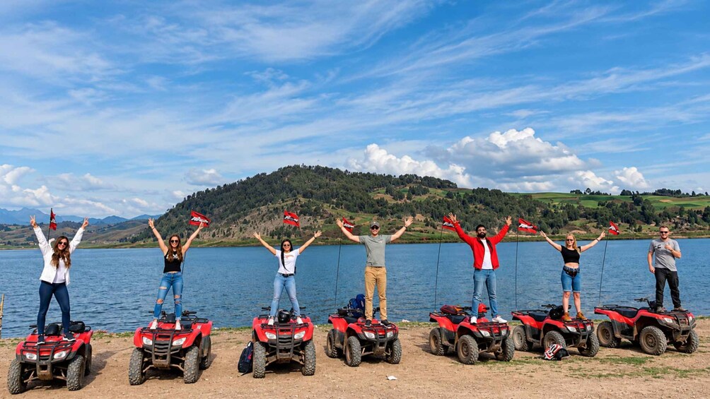 A group of people on ATVs by a lake with a mountainous backdrop. 1