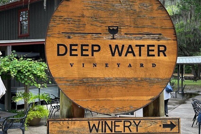 A wooden sign for Deep Water Vineyard with a wine glass icon and an arrow pointing right. 2