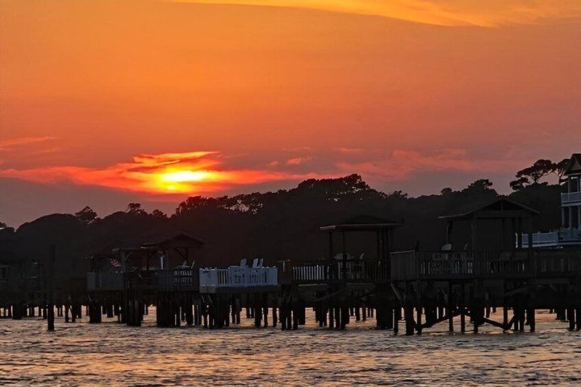 A sunset over a waterfront with wooden structures and trees in the background. 2