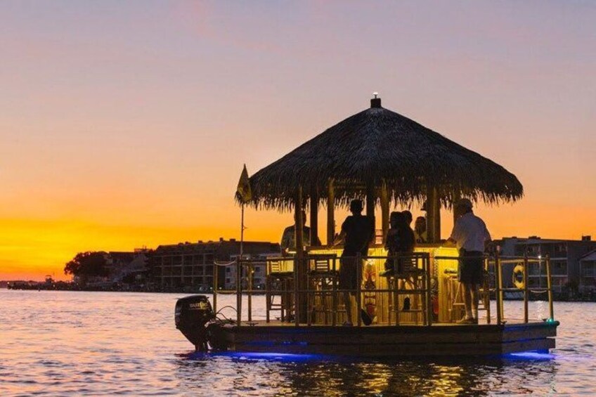 A boat with a thatched roof and people on it, floating on water during sunset. 1