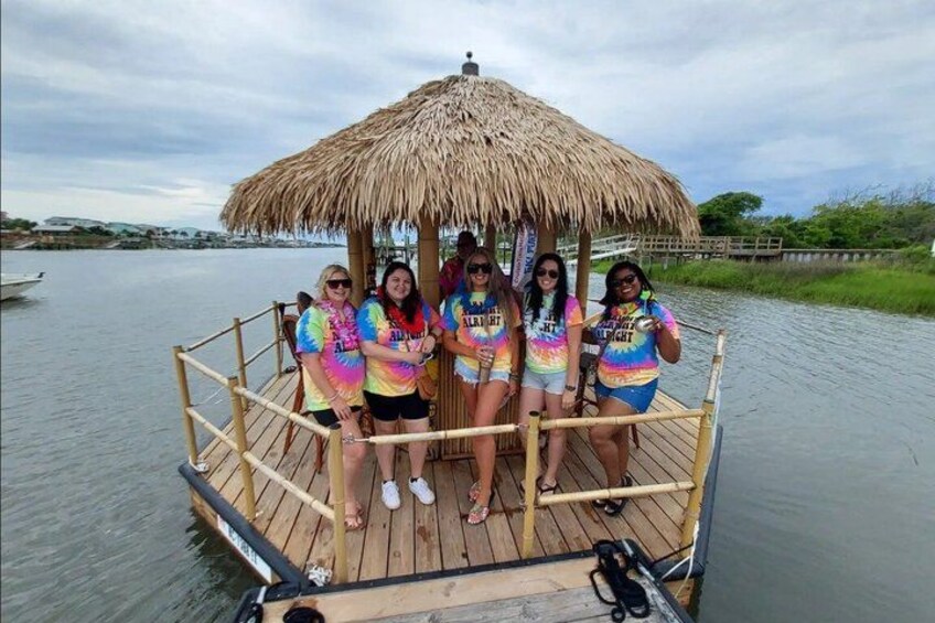 A group of people on a wooden boat with a thatched roof, surrounded by calm water and greenery. 2