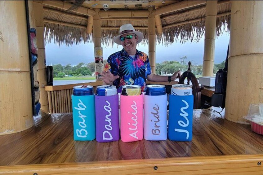 A person standing in a wooden structure with a thatched roof, holding a drink, and surrounded by colorful containers labeled with names. 5