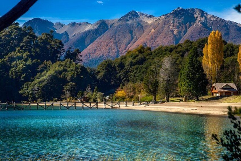 A lake with clear water, a wooden dock, a house, and mountains in the background. 2