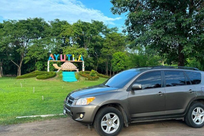 A gray SUV parked in front of a sign with the word 'AYUTLA' and a stylized turtle graphic. 2