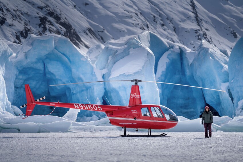 A red helicopter with the registration number N99605 parked on snow in front of a glacier. 4