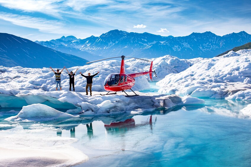 A red helicopter on a glacier with three people standing nearby. 1