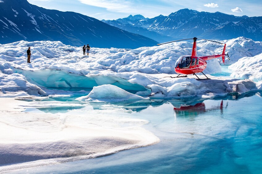 A red helicopter on a frozen lake with people walking in the background and mountains in the distance. 3