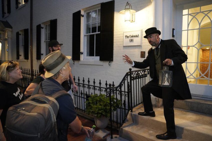 A person in a black coat and hat standing on a staircase, holding a lantern. 1