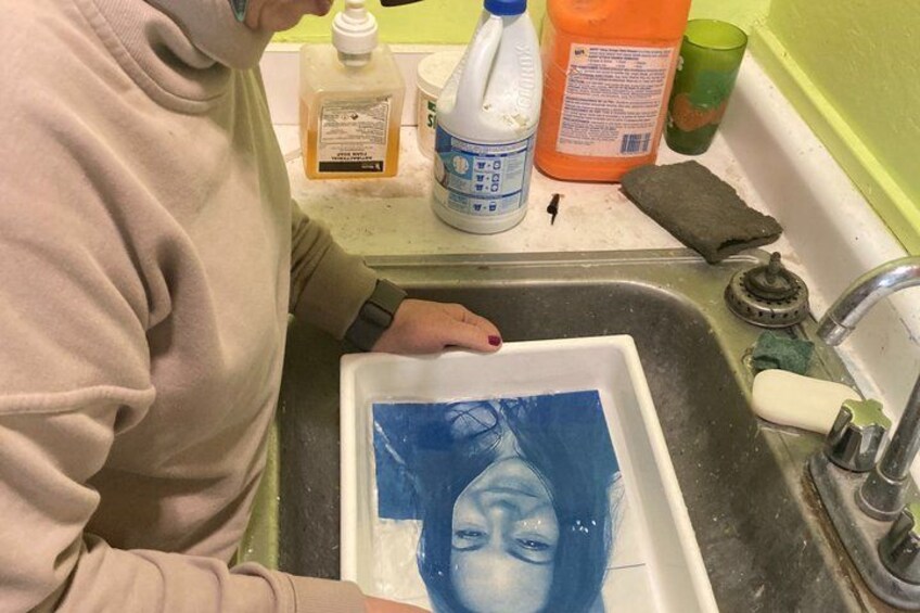 A person washing a blue object in a sink with various cleaning products on the counter. 3