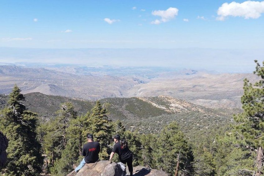 Two people sitting on a rock with a mountainous landscape in the background. 4
