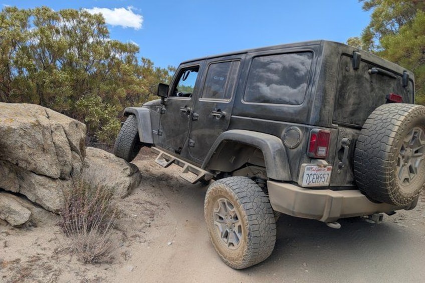 A rugged off-road vehicle parked on a dirt path with large tires, surrounded by rocks and sparse vegetation. 3