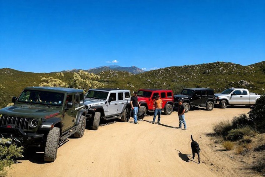 A group of off-road vehicles parked on a dirt road with a mountainous landscape in the background. 1