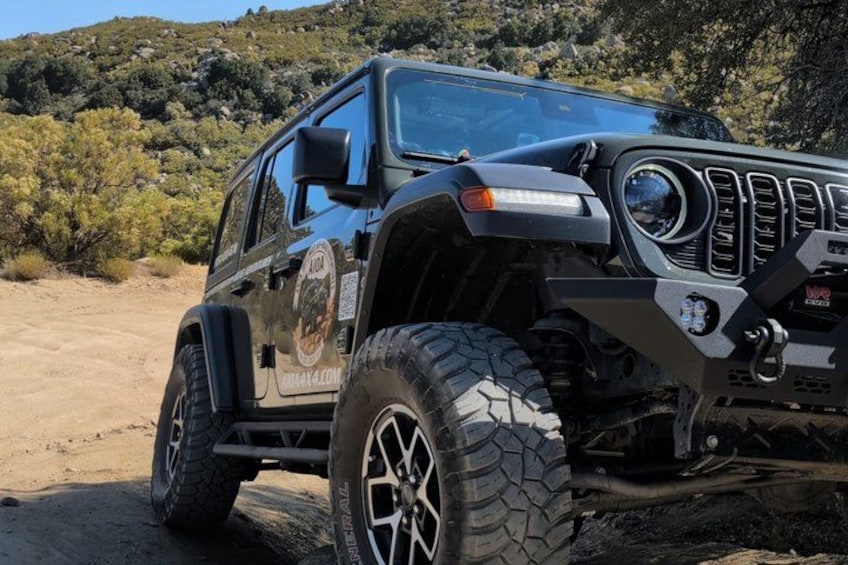 A black off-road vehicle with large tires and a rugged design, parked on a dirt path with a mountainous background. 4