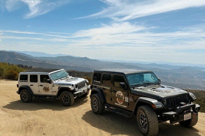 Two off-road vehicles on a dirt road with a mountainous landscape in the background. 3