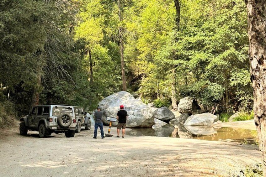 A Jeep navigating a dirt path, surrounded by large boulders and dense forest. 2