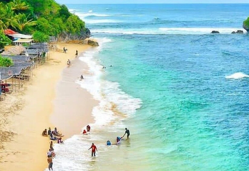 A beach with people swimming and walking along the shore, palm trees, and a clear blue ocean. 5