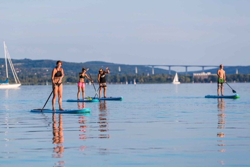 People paddleboarding on calm water with a bridge and hills in the background. 5