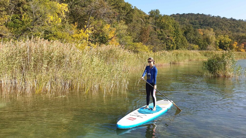 A person paddleboarding on a calm river surrounded by autumn foliage. 3