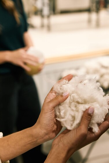 A person holding a fluffy white material, likely cotton or wool, with another person in the background holding a container. 4