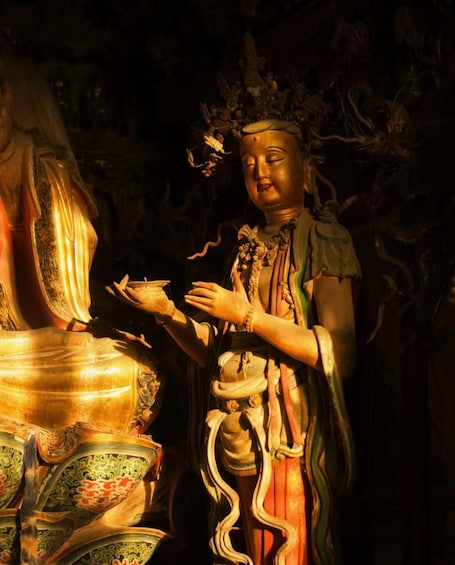 A statue of a figure with a serene expression, adorned with traditional attire and jewelry, standing in a dimly lit environment. 3