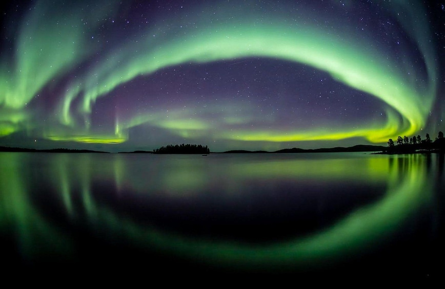 The Northern Lights over a calm lake with a silhouette of trees and a distant landmass. 5