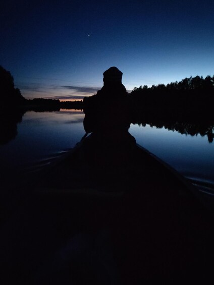 A silhouette of a person on a boat at dusk with a calm lake and a mountain in the background. 3